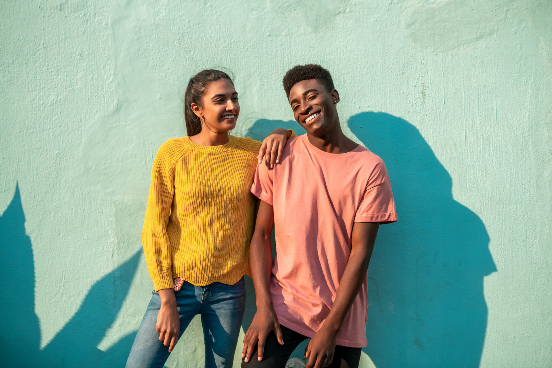 Two people standing and smiling by a green wall